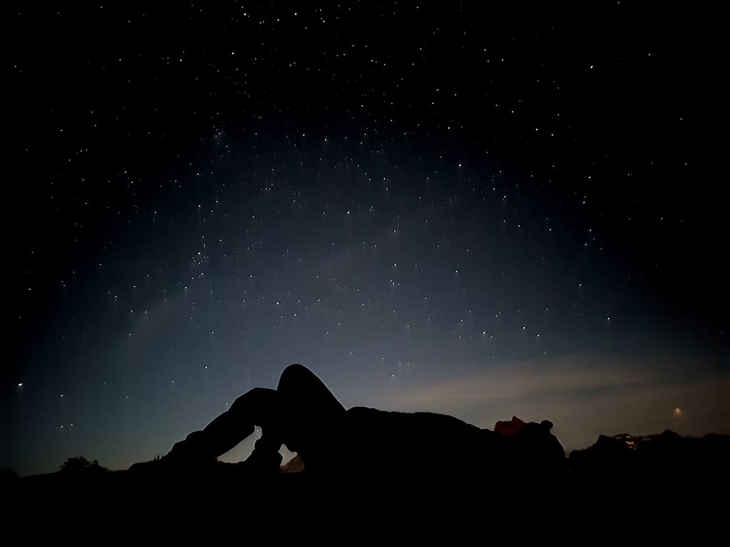 A silhouette of a girl lying on her back and looking at the stars