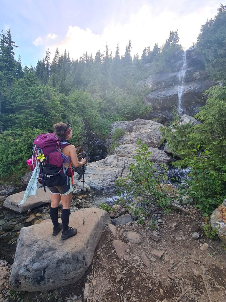 A waterfall along Gothic Basin Trail in Verlot Washington, Girl facing waterfall wearing backpack