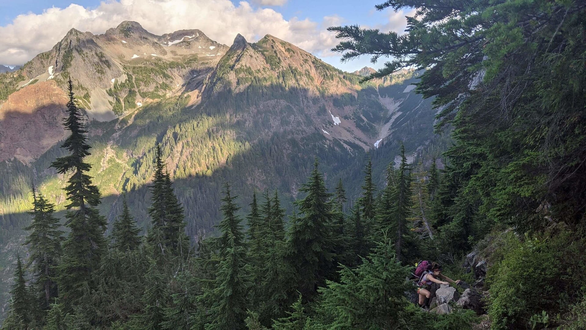 Girl climbing along a tree-covered trail, cascade mountains in the distance, gothic basin trail